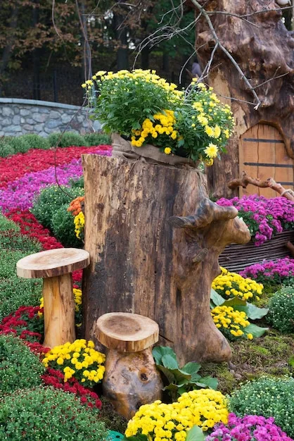 A vibrant garden bed filled with a variety of colorful flowers and lush green plants. The garden bed is bordered by natural stones, and there is a small wooden sign identifying the plant names.