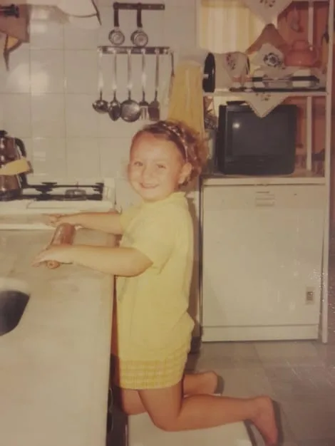 Close up shot of a clear, adhesive child safety lock on a kitchen cabinet, preventing a child from opening it. The background shows blurred kitchen utensils and dishes.